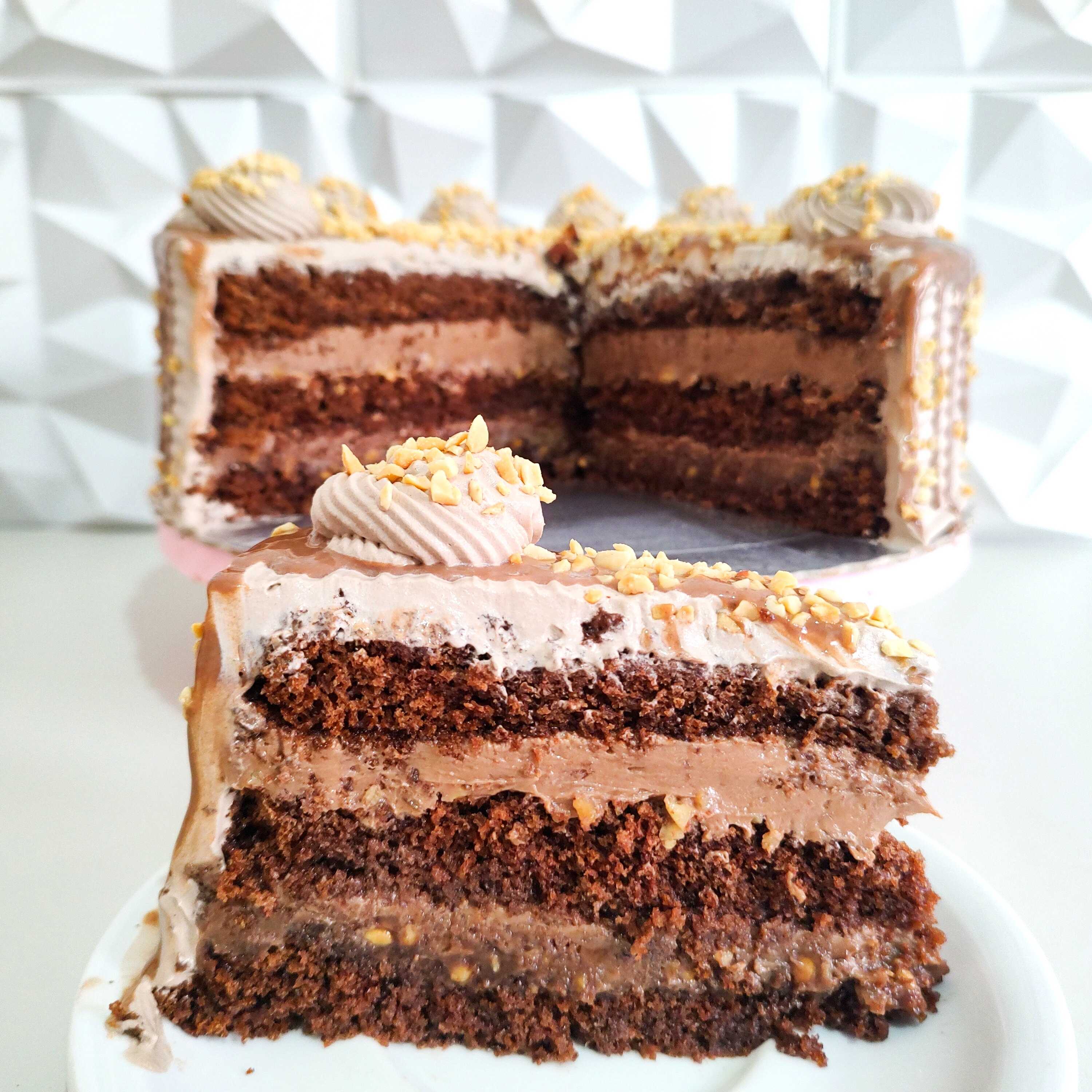 Fatia de Torta Ferrero Rocher: Uma explosão de chocolate em cada camada: massa fofinha, brigadeiro trufado, brigadeiro ao leite e ganache com amendoim. Cremosa, intensa e simplesmente impossível de resistir.