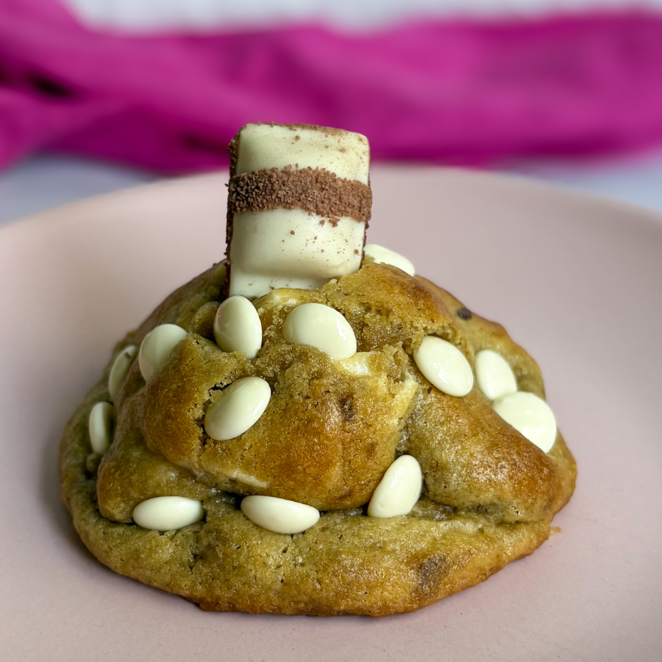 Assado na hora, com cerca de 120g. Massa tradicional com gotas de chocolate branco, recheado com creme de Kinder e finalizado com um pedaço de Kinder Bueno White por cima. É macio por dentro e crocante por fora