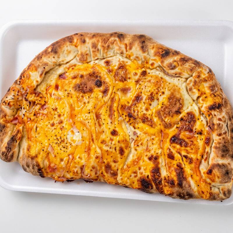 A 'Fogazza Portuguesa' da nossa categoria de 'Fogazzas' é deliciosamente recheada com presunto finamente picado, acrescentando uma textura única e sabor inconfundível. Adicionamos a suavidade da mussarela derretida, que harmoniza perfeitamente com o toque cebola. Por fim, o ovo, preparado com maestria, finaliza este prato com uma dose extra de sabor e personalidade.