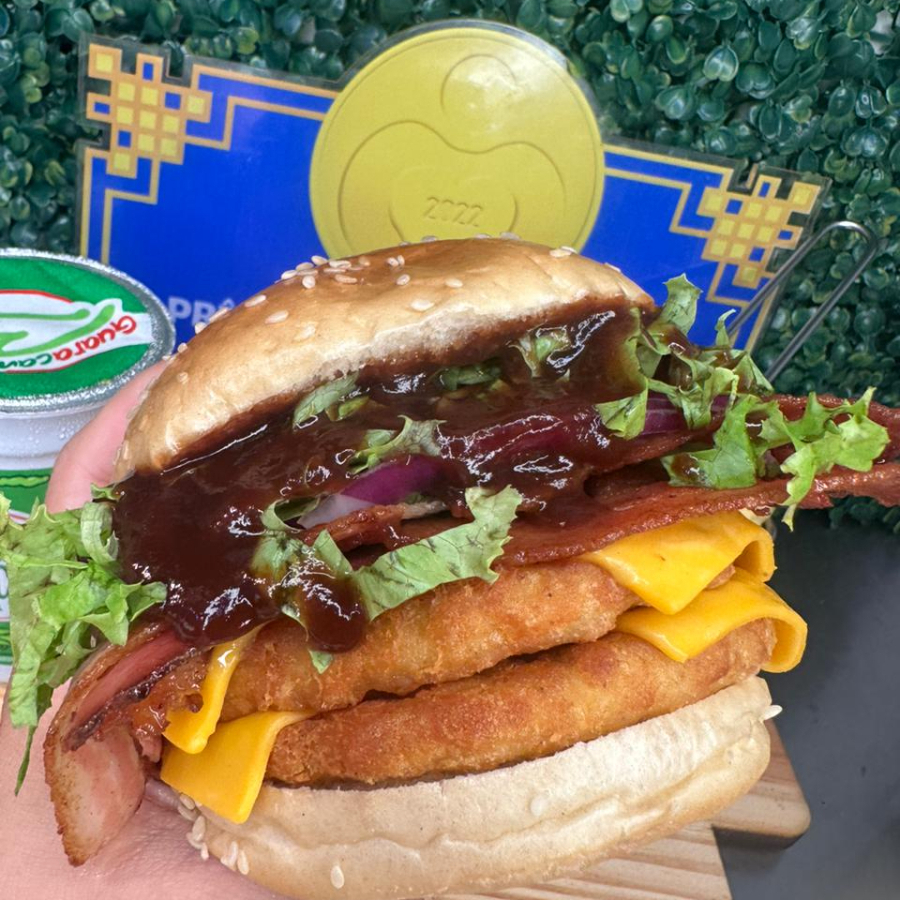 Pão, 2 hamburguer de frango empanado, queijo chedar, fatias de bacon, cebola roxa, alface e barbecue.