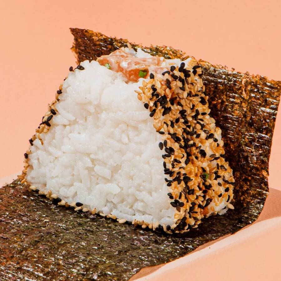 Bolinho de arroz Shari, recheado com salmão, cream cheese, teriyaki e cebolinha, envolto por um mix de gergelim e acompanhado de alga nori, embalada separadamente para manter a crocância até o momento de consumo.