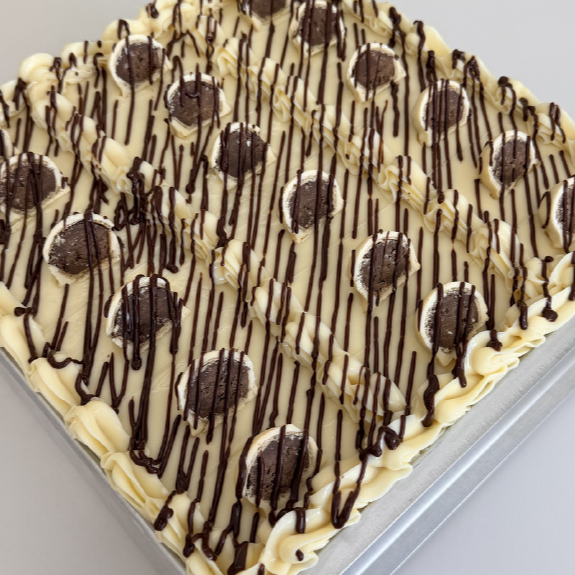Bolo de massa branca aromatizado com pasta de baunilha, recheado com Creme de Chocolate com pedaços de bombom Ouro Branco e cobertura de Creme de Ninho