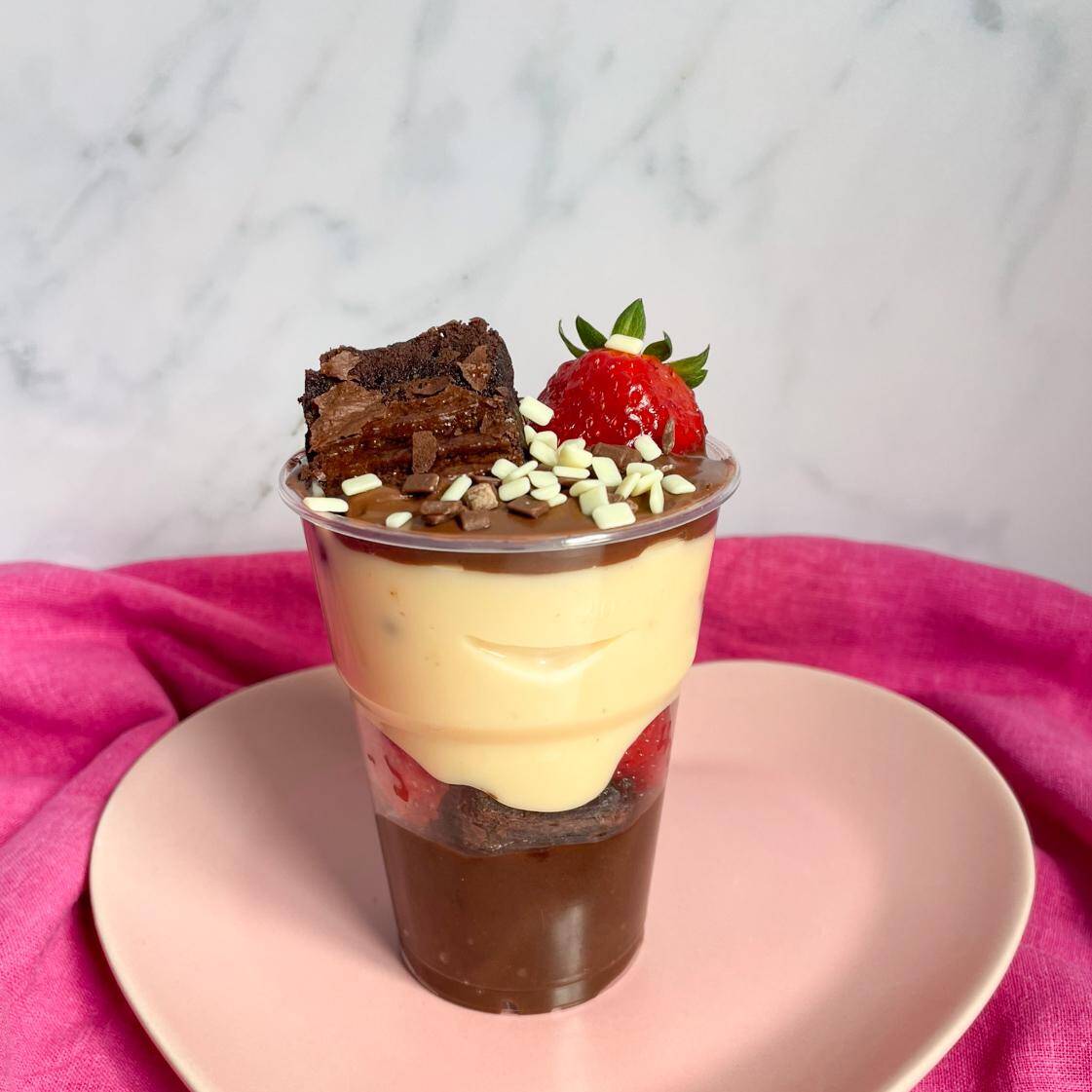 Nosso copo da felicidade é composto por uma camada de brigadeiro de chocolate cremoso, brigadeiro Ninho, pedaços do melhor brownie do mundo e morangos frescos cortados. Finalizado com Nutella, brownie, um morango inteiro e granulé de chocolate branco e preto.