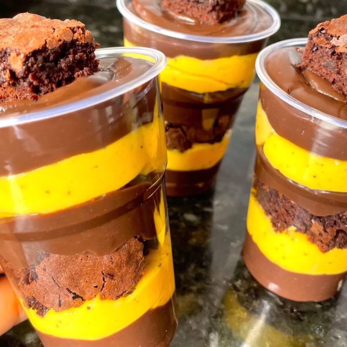 Sobremesa deliciosa montada no copo, composta de camadas brigadeiro cremoso de chocolate ao leite e brigadeiro de maracujá, lasquinhas de brownie e mousse de chocolate para finalizar