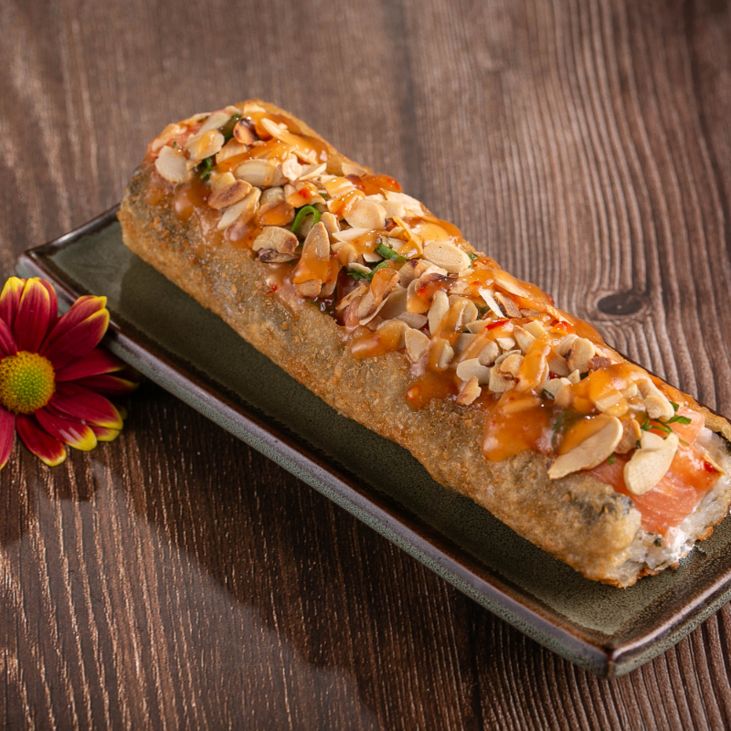 Hot empanado cortado ao meio com recheio de cream cheese, salmão em cubos, coberto com laminas de amêndoas e finalizado com molho de pimenta, cebolinha e gergelim.