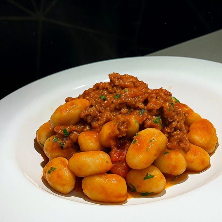 Gnocchi de batatas, envolvido ao molho bolonhesa e ervas frescas.