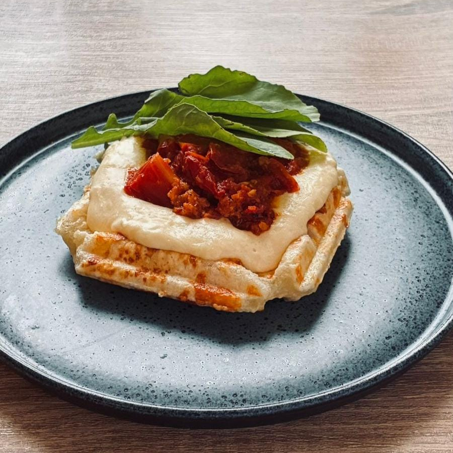 Waffle de pão de queijo, tomate confit e rúcula.