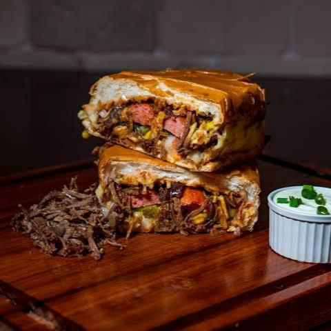 Prepare o seu paladar para uma experiência única. Nossa costela é assada lentamente até desmanchar, servida em um pão super macio com tomates frescos picadinhos e cebola crocante. Para finalizar, aquela generosa camada de batata palha que garante o "crunch" perfeito a cada mordida. É a união perfeita da tradição do hot dog com o sabor rústico da costela de verdade!"