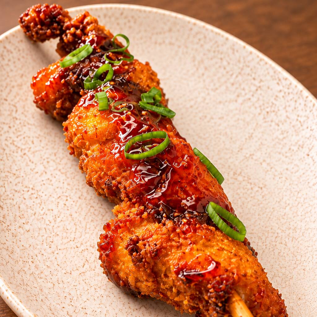 1 Espetinho (150g) de peito de frango temperado com especiarias coreanas empanado com farinha panko, frito e depois pincelado com molho de laranja picante.