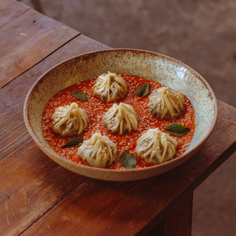 Dumplings delicadamente cozidos, recheados com portobello e tofu defumado, servidos sobre um molho caseiro quente de tomate com especiarias e creme de castanha de caju defumada, finalizados com gergelim branco torrado.