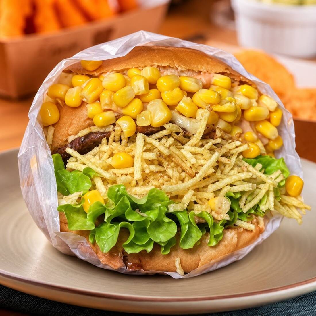 Pão com burguer 100g, muçarela, tomate, alface, milho e batata palha. Um lanche leve, bem montado e saboroso.