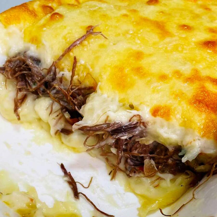 Escondidinho de Macaxeira recheado com carne de sol refogada e temperada ao ponto e gratinada com queijo mussarela. Acompanha Arroz Branco
