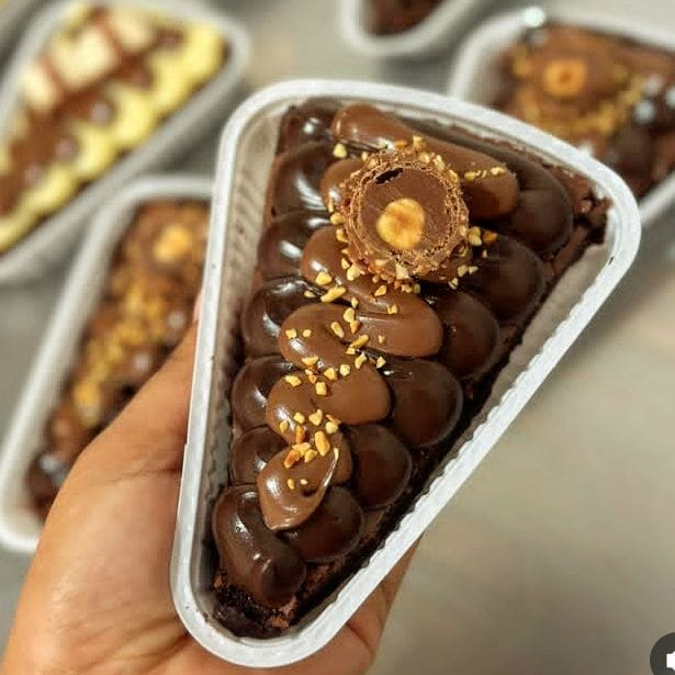 Fatia do nosso delicioso brownie molhadinho coberto de chocolate ao leite, Nutella pura e finalizado com amendoim triturado e 2 brigadeiros gourmet de ferrero rocher.