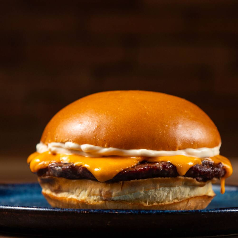 Pão brioche, hambúrguer artesanal suculento (100g), ketchup americano, 2 fatias de cheddar, ketchup e maionese.