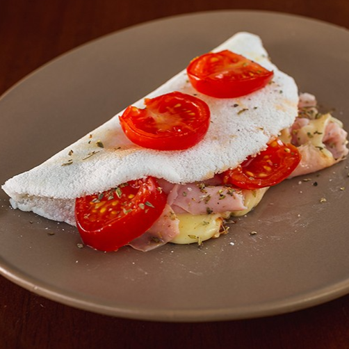 Recheada com presunto saboroso, queijo à sua escolha (minas, coalho, mussarela, requeijão ou cheddar), tomate cereja fresquinho e um toque especial de orégano que perfuma e realça o sabor. Perfeita para quem ama pizza, mas não abre mão da leveza e do sabor único da nossa massa de tapioca.
