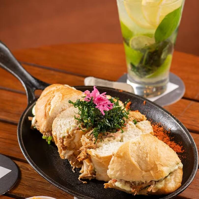 Pão baguete crocante recheado com pernil desfiado, macio e bem temperado, maionese especial de ervas e vinagrete fresquinho. Um sanduíche artesanal bem servido, suculento e cheio de sabor.