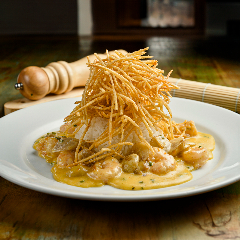 Camarões servidos em um molho cremoso (espumante), com adição de uvas, e acompanhados por arroz branco e batata palha da casa.