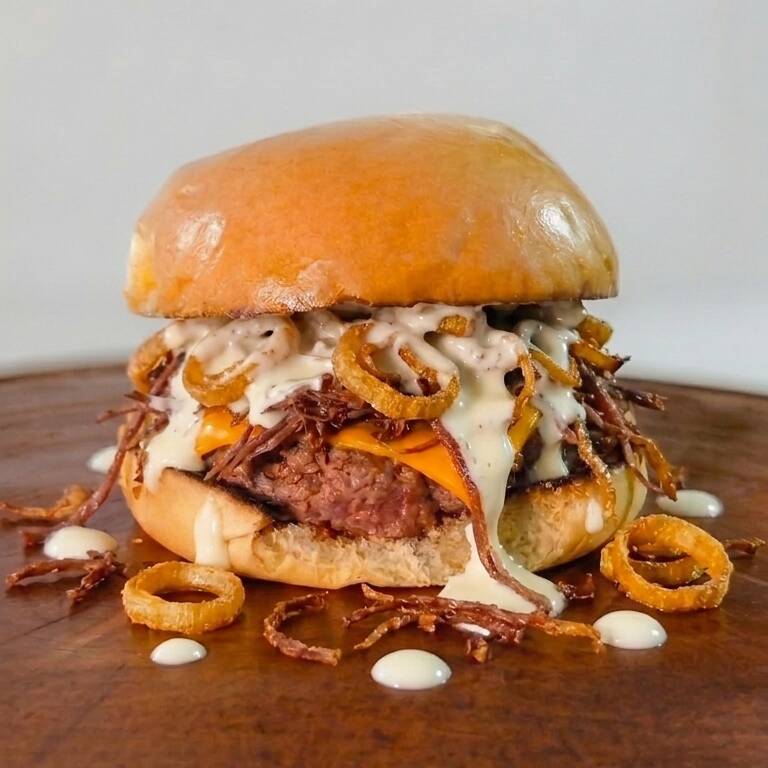 Pão brioche macio e selado na manteiga, burger artesanal suculento de 180g, duas fatias de queijo cheddar derretido, bastante carne seca desfiada e o toque final inconfundível dos anéis crocantes de alho-poró frito. Uma verdadeira tentação de sabores e texturas!