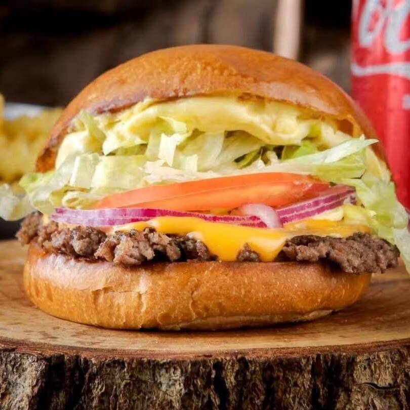 Pão brioche, Blend Angus 160g na brasa, cheddar, alface, tomate e cebola roxa.