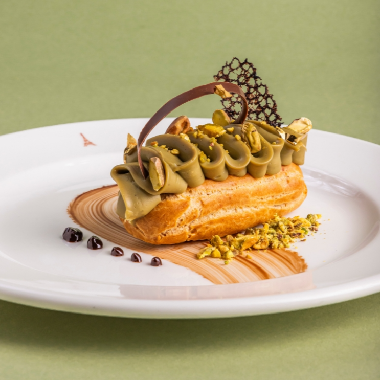 Deliciosa Éclair, com massa leve e dourada, coberta com ganache de pistache. Recheada com ganache de chocolate belga meio amargo e finalizada com farofa de pistache.