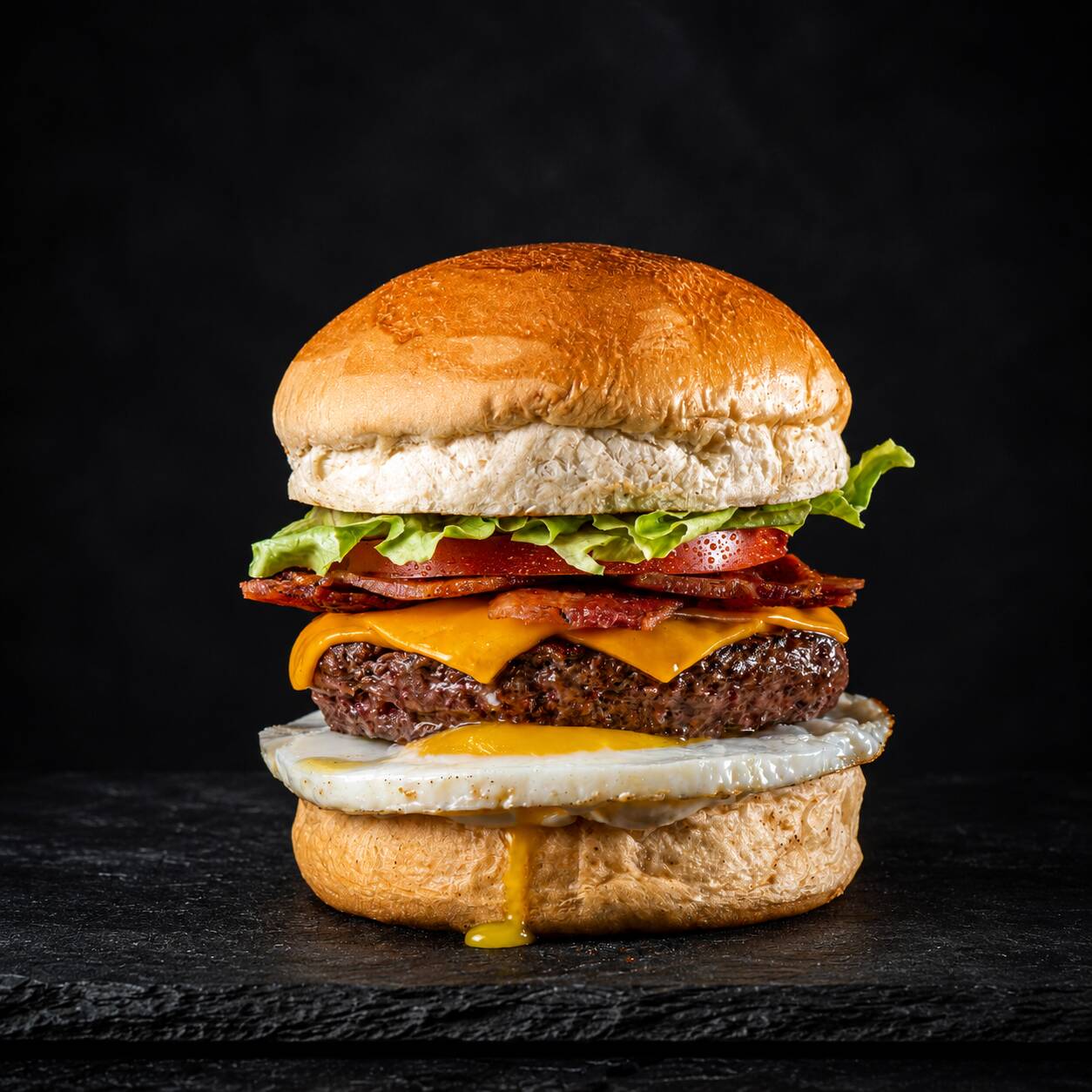 Pão brioche, 180g de alcatra moída com bacon, alface, tomate, cebola, queijo cheddar, ovo e molho especial loyola.