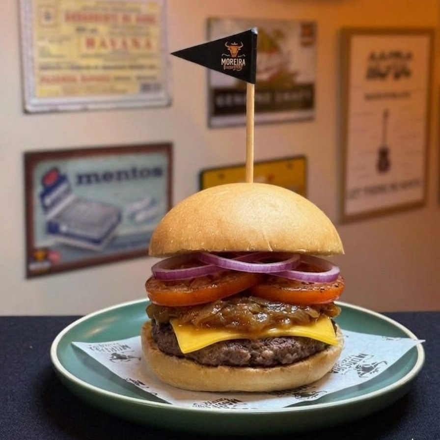 Suculento Burger Angus, Fatias de Queijo Cheddar Americano, Cebola Caramelizada, Tomate Chapeado, Molho Barbecue Artesanal, Mostarda. Servido no Pão Levemente Selado