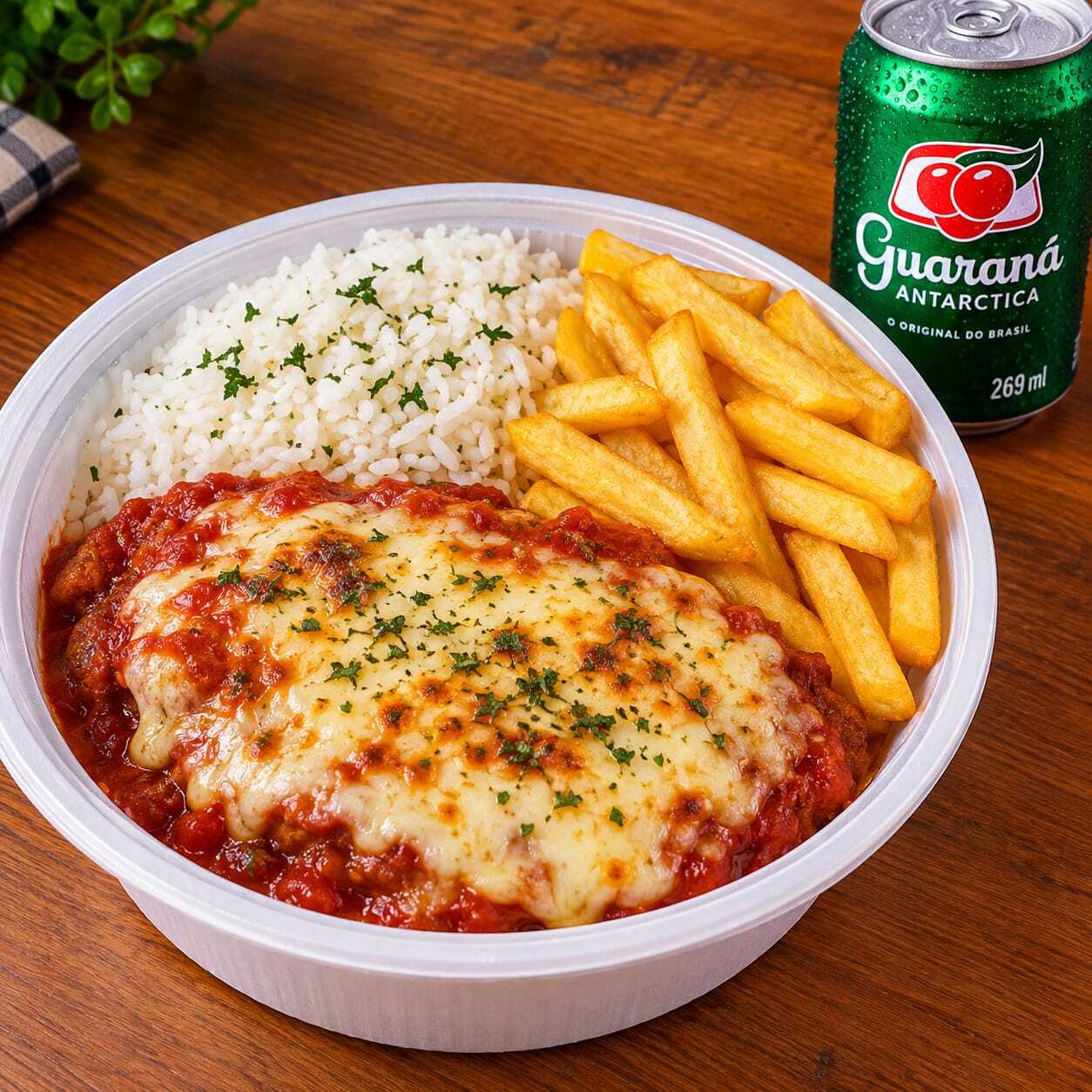 Marmita com bife à parmegiana, coberto com molho de tomate e queijo derretido, acompanhada de arroz e batata frita. Para completar, Guaraná lata 269ml aproximadamente 600g.