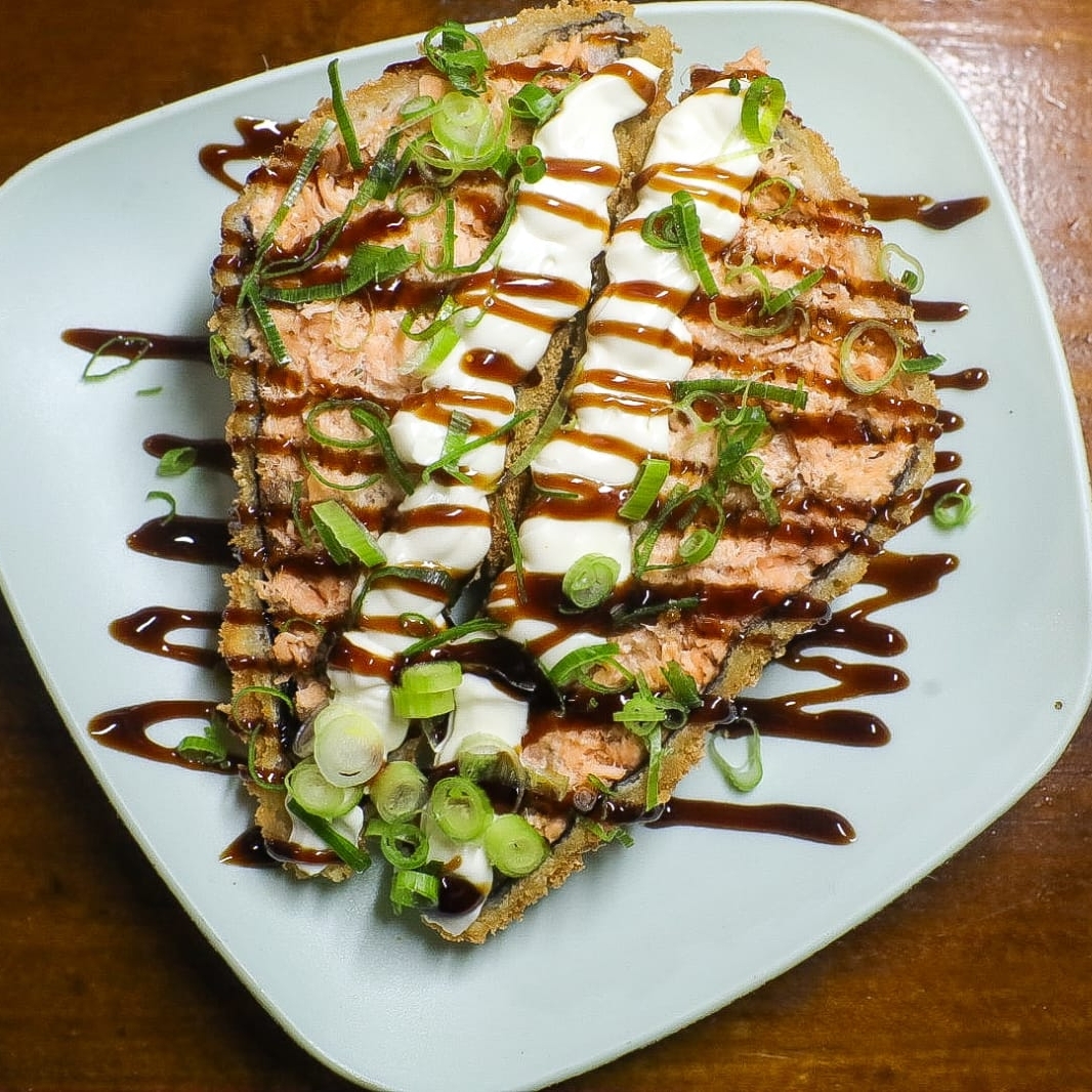 Temaki de salmão grelhado, empanado e frito, cortado ao meio e recheado com cream cheese, finalizado com molho tarê e cebolinhas. Uma combinação deliciosa que traz frescor e crocância em cada pedaço.
