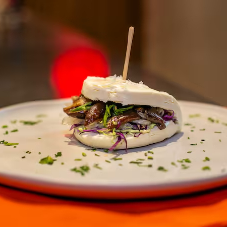 O Vegan Bao é uma opção leve e cheia de umami, combinando ingredientes frescos e sabores intensos dentro de um pão bao macio e vaporoso. Ingredientes: Pão bao fofinho e levemente adocicado. Shiitake salteado, trazendo uma textura suculenta e um sabor terroso e umami marcante. Salada crocante, adicionando frescor e equilíbrio ao recheio. Picles de cebola, que proporciona acidez e contraste ao sabor intenso do shiitake. Cebolinha fresca, dando um toque aromático e leveza ao conjunto. Molho Teriyaki, agridoce e encorpado, realçando todos os sabores com um toque caramelizado. O Vegan Bao é uma combinação equilibrada de texturas e sabores, ideal para quem busca uma opção vegana cheia de personalidade e deliciosa!