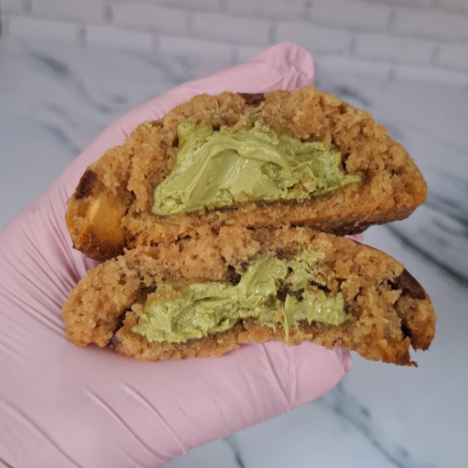 Cookie feito com massa de baunilha, chocolate branco, chocolate preto e recheado com um delicioso creme de pistache