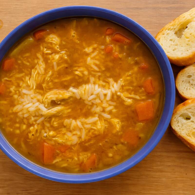 Caldo de legumes com legumes em cubos, frango desfiado e torradas de acompanhamento.
