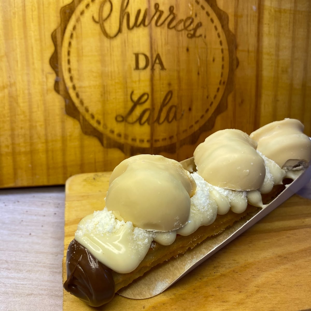 massa fresca, artesanal, feita todos os dias, bem fritinho e crocante, envolvido em açúcar e canela, com um delicioso recheio de nutella dentro, e fora de leite ninho, finalizado com bombons de ouro branco