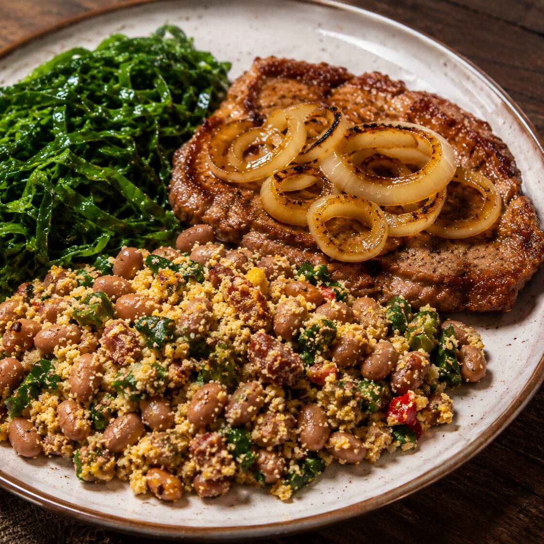 Feijão tropeiro tradicional, rico em temperos marcantes, servido com a leveza da couve refogada na medida certa. Para acompanhar, um bife de porco macio e dourado na chapa, coberto por generosas rodelas de cebola amaciadas no próprio suco da carne. Uma combinação caseira cheia de sabor, textura e aroma reconfortante que entrega uma refeição completa, quente e extremamente satisfatória para o seu almoço.