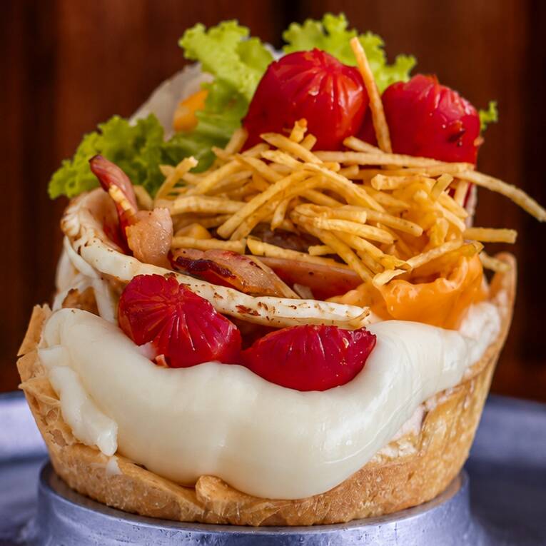 Pão macio com hambúrguer suculento, muçarela, presunto, bacon crocante, salsicha, Catupiry cremoso, alface, tomate, milho verde e batata palha. Completo e irresistível.