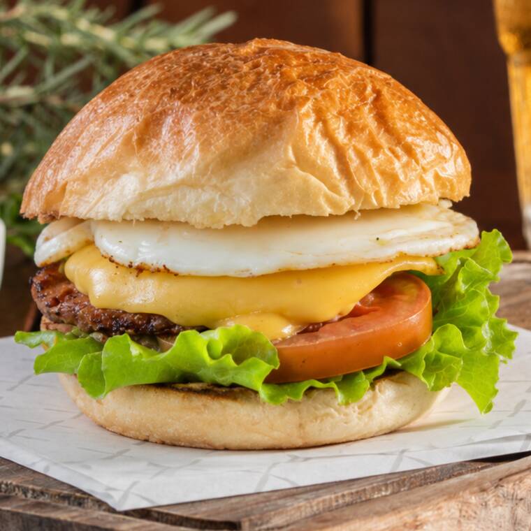 Hambúrguer suculento, queijo derretido, alface crocante, tomate, ovo frito, no pão brioche.