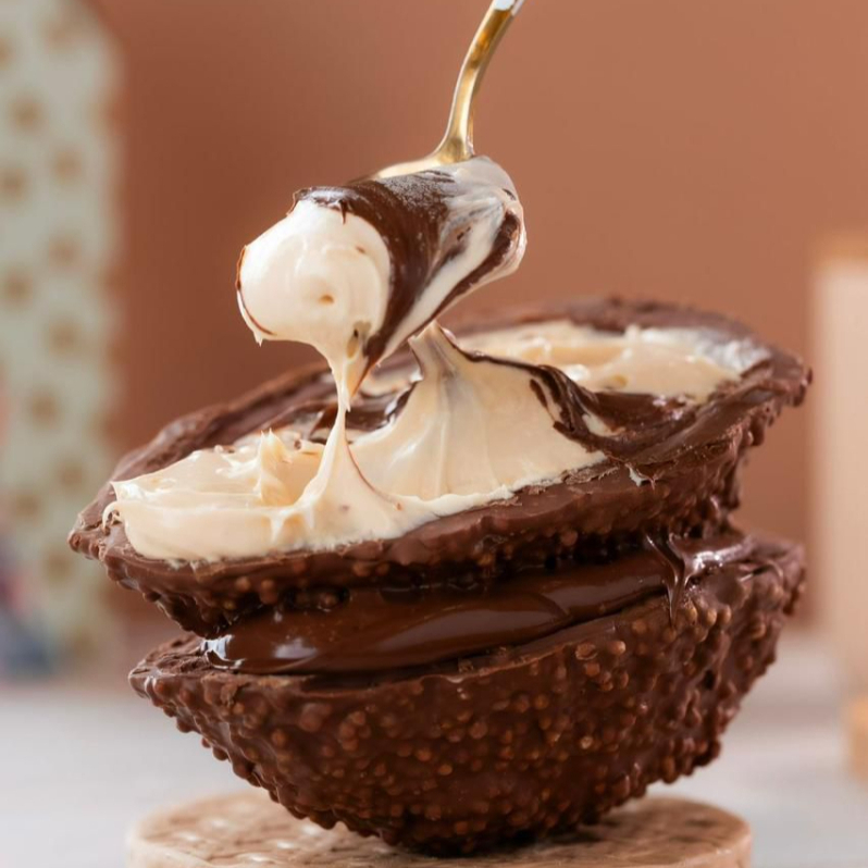 Casca de chocolate belga com flocos de arroz crocrante, recheada com Nha Benta suave de Ninho e Nutella cremosa em camadas generosas. Leve, doce e indulgente. Aprox. 610g