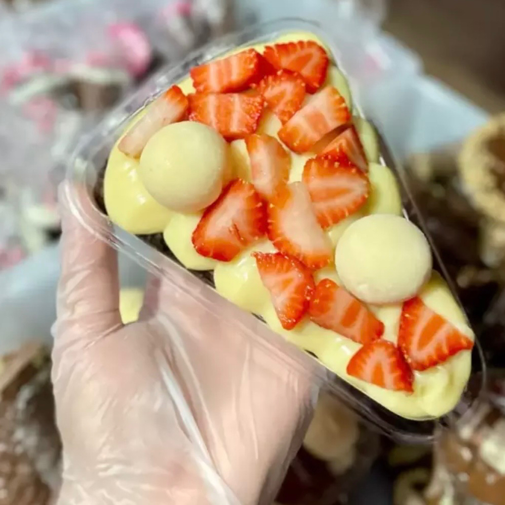 Fatia de Brownie com cobertura de brigadeiro de ninho, morangos picados e dois docinhos de ninho.