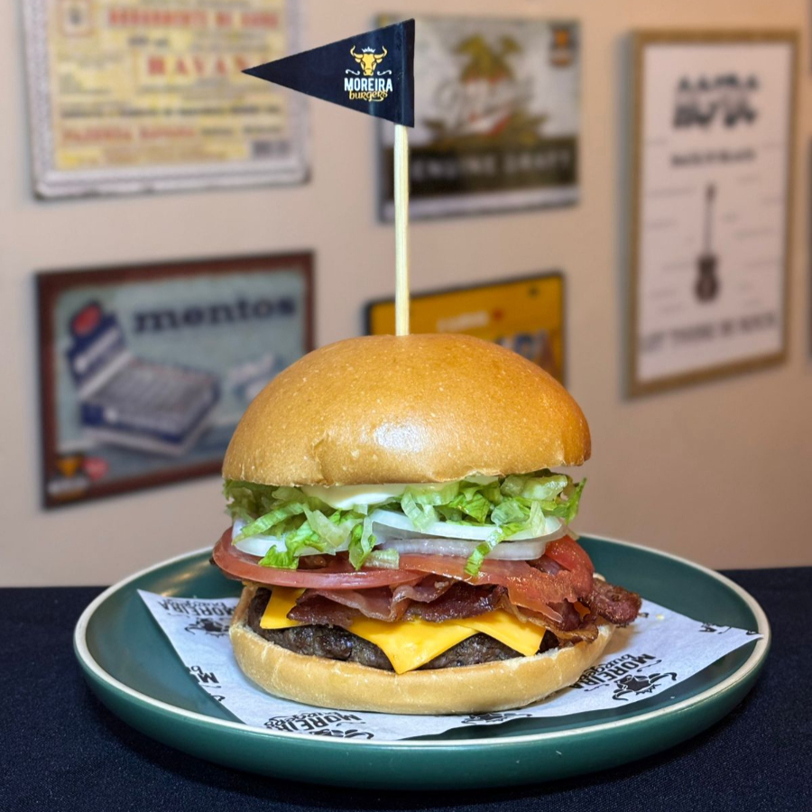 Suculento Burger Angus, Fatias de Queijo Cheddar Americano, Alface Americana Picado, Fatias de Bacon Crocante, Cebola Crua, Tomate, Ketchup, Maionese. Servido no Pão Levemente Selado