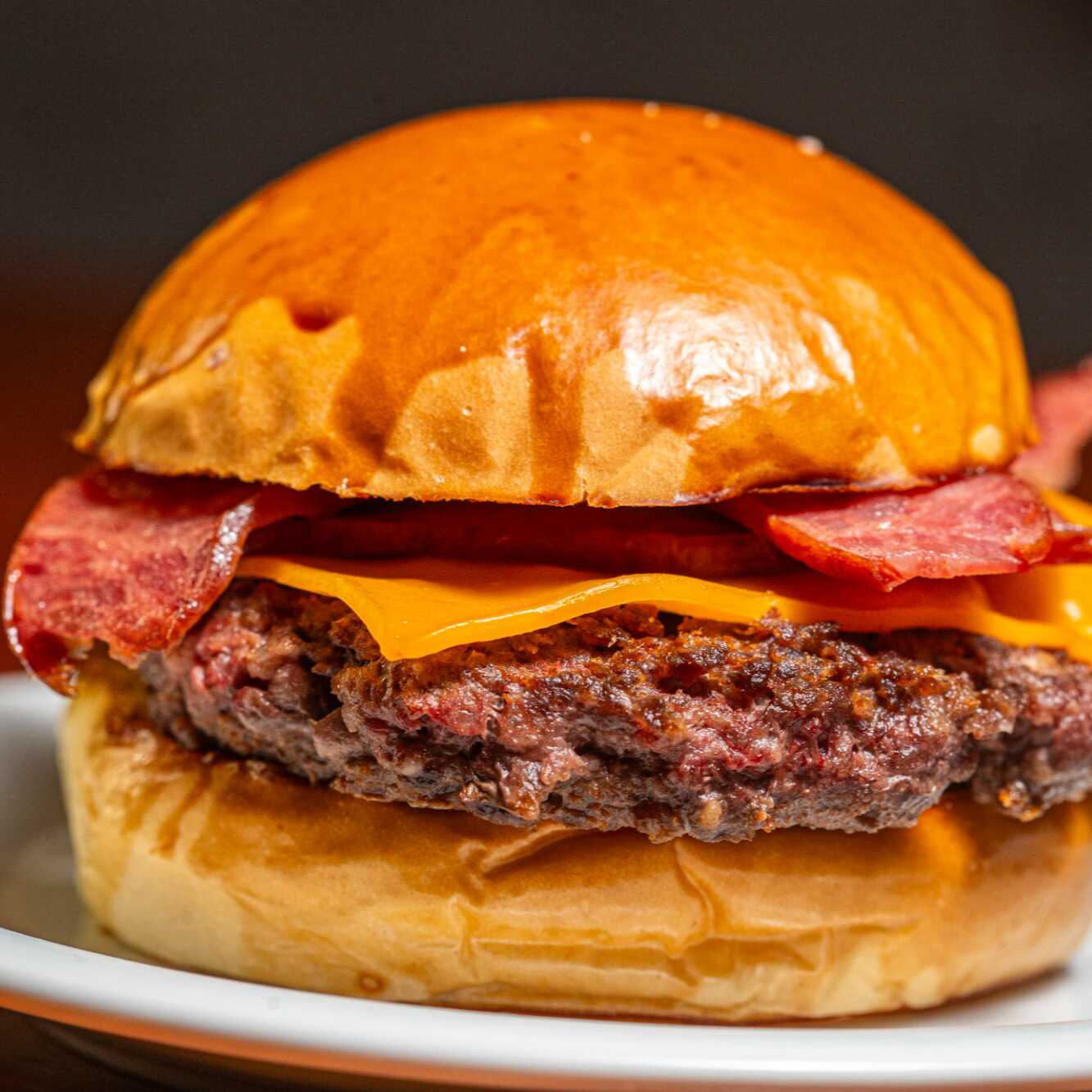 Blend bovino de 180g grelhado na brasa, suculento e com aquele sabor marcante de churrasco. Coberto com queijo prato bem derretido, bacon crocante em generosa quantidade e finalizado com a maionese da casa.
Servido no pão brioche levemente tostado, macio por dentro e com leve crocância por fora.
Combina perfeitamente com uma Coca-Cola Zero Lata 350ml bem gelada.