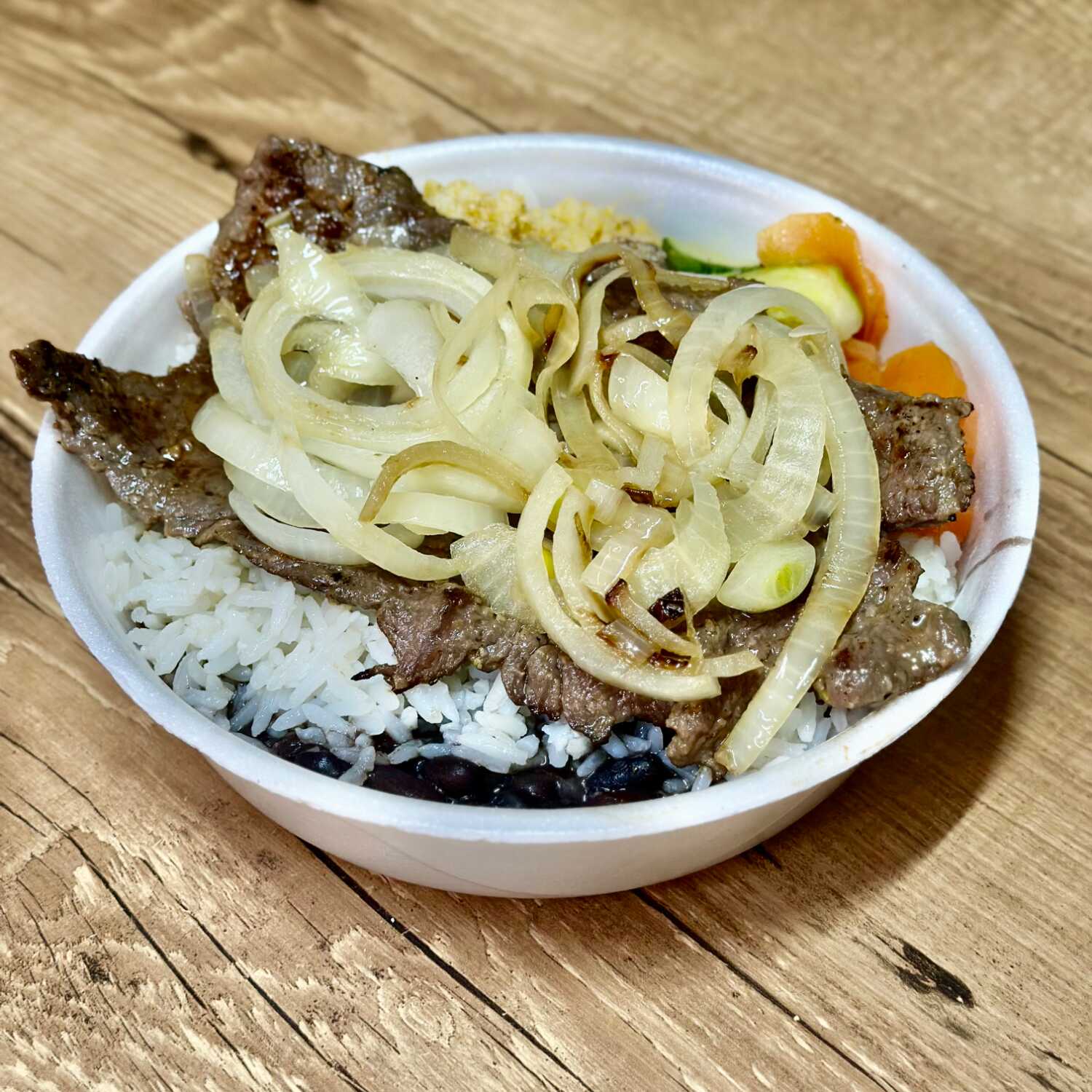 Bife com tempero especial grelhado na chapa coberto por uma camada cebola, acompanhado de arroz, feijão, farofa caseira e legumes refogados