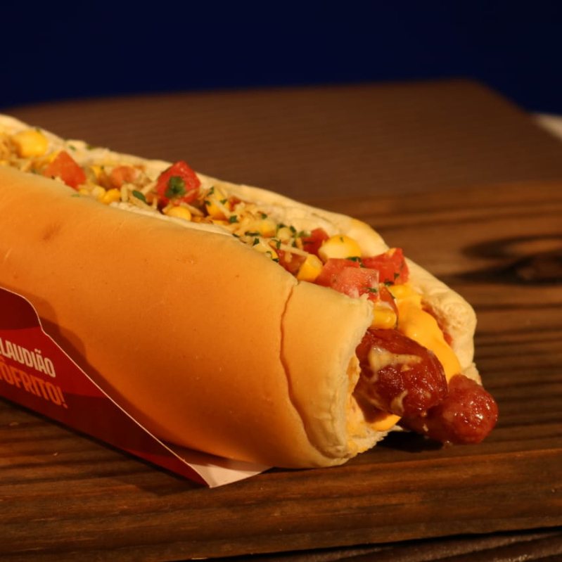 Pão, 2 linguiças picantes, molho de tomate, molho cheddar, maionese, ketchup, mostarda, molho mil ilhas, tomate, milho, ervilha, salsa, queijo parmesao e batata palha.