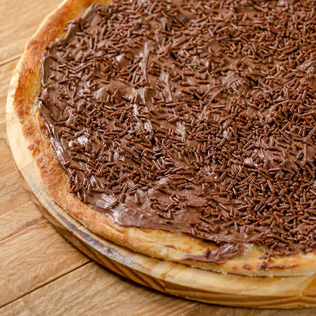 Base de creme de leite e uma porção generosa de chocolate ao leite espalhado por toda a pizza, finalizado com granulado crocante por cima.
