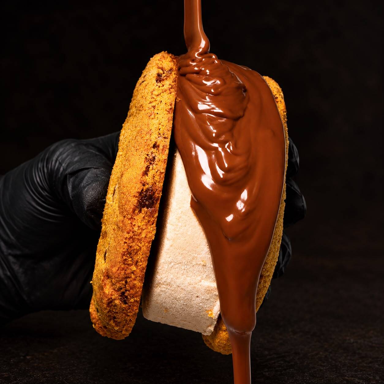 Dois cookies irresistíveis envolvendo uma generosa camada de gelato/sorvete artesanal de baunilha recheado com sabor da sua escolha, finalizados com uma deliciosa ganache de chocolate. Uma combinação perfeita de texturas e temperaturas: a intensidade do cookie, a cremosidade do gelato e o toque chocolatudo que transforma cada mordida em uma experiência única.