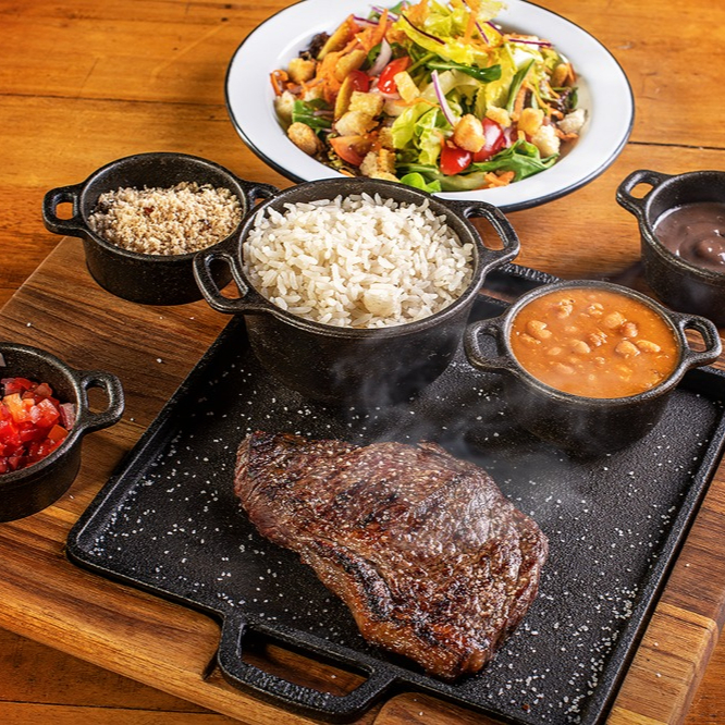 180g de Bife Ancho Angus in natura. - Entrada: Porção da nossa salada mix de folhas. - Acompanha Arroz e Vinagrete. - Sobremesa: brigadeiro de colher. Não enviamos talheres de plásticos. Caso queira os outros itens, adicionar nos complementos.