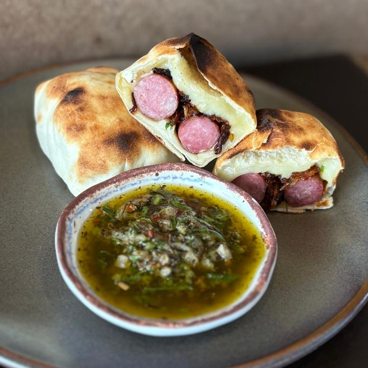 Massa fina e macia envolvendo linguiça de cordeiro, mozarela derretida e crocantes cebolas fritas, servida com um acompanhamento especial de Chimichurri árabe. Sabor marcante, textura leve e perfeita para comer com as mãos. Caso deseje descartáveis ou temperos (sal, limão ou azeite), solicite no momento do pedido.