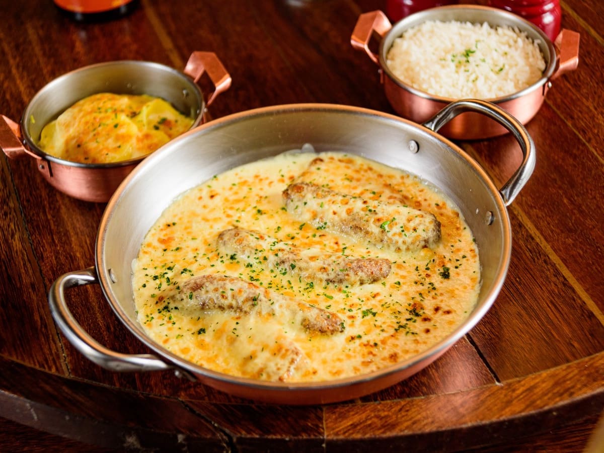Tilápia com bananas fritas e molho branco, gratinado com queijos muçarela e parmesão. Acompanha arroz branco e batatas gratinadas.