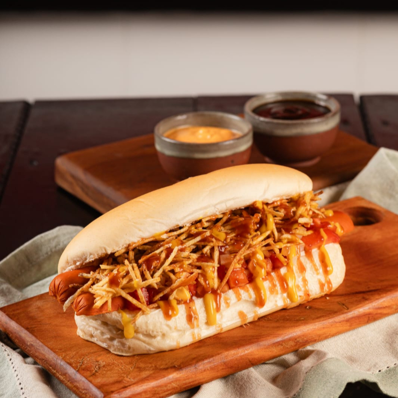 Pão prensado na chapa, 2 salsichas(PERDIGAO), salada de milho, tomate, cebola, batata palha, mostarda e ketchup.