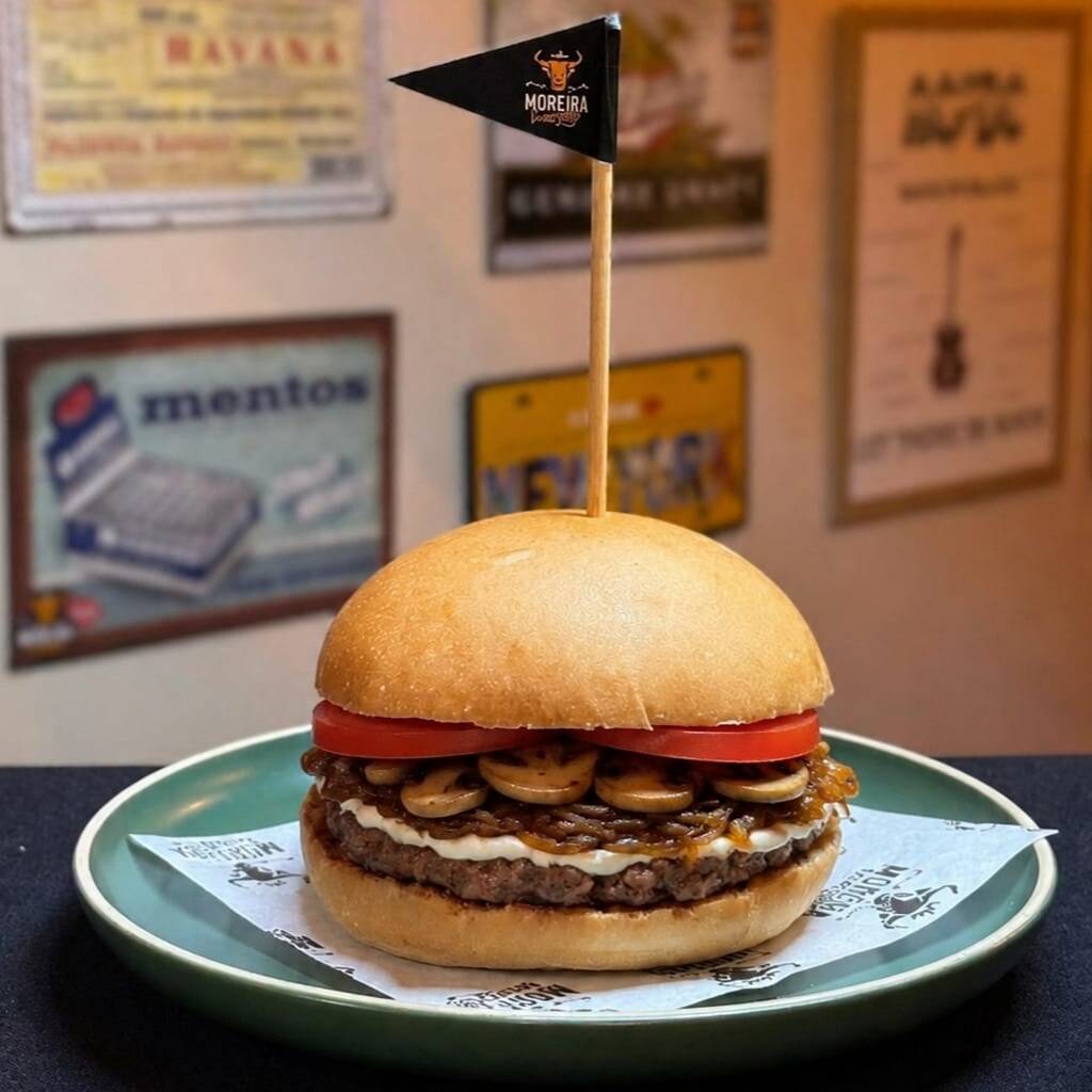 Suculento Burger Angus, Requeijão Cremoso, Champigon Selado na Manteira de Garrafa, Cebola Caramelizada, Tomate, Mostarda, Maionese. Servido no Pão Levemente Selado