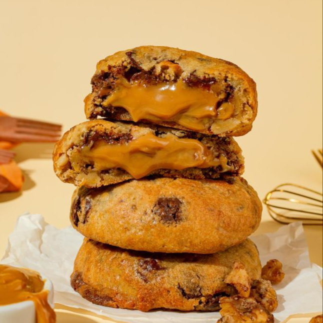 Um Cookie Doce de Leite com Nozes é um biscoito feito com uma massa tradicional de cookie, geralmente amanteigada, enriquecida com pedaços crocantes de nozes e recheada com doce de leite cremoso e artesanal, oferecendo uma combinação de texturas e sabores, com a massa macia ou crocante e o recheio doce e a riqueza das nozes