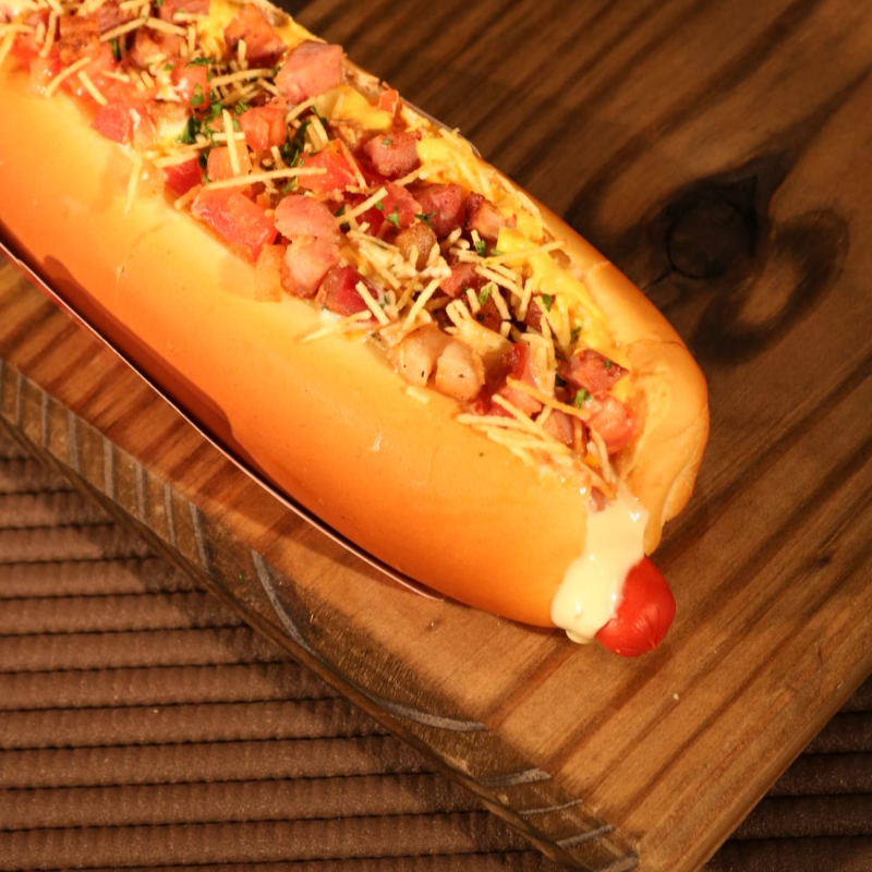 Pão, salsicha, molho de tomate, molho cheddar, bacon, maionese, ketchup, mostarda, molho mil ilhas, tomate, milho, ervilha, salsa, queijo parmesão e batata palha.